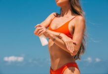 Kobieta w pomarańczowym bikini nakłada krem z filtrem na plaży